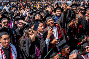 Group of graduates in black caps and gown standing with their phones poised for photos.