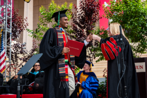 Student in cap and gown exchanges fist bump with CSUN President Erika D. Beck on commencement stage