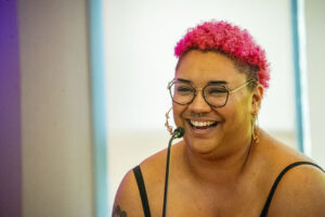 Whitney Workman, manager of the CSUN Pride Center, laughs and stands behind a podium microphone.