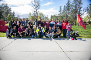 A large group of students pose together near the University Library lawn.