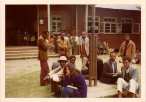 Andi Ostrowe sits outside a building, surrounded by several men.