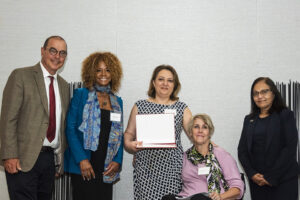 Group poses for the camera. Doris Abrishami is in the center, holding her award.