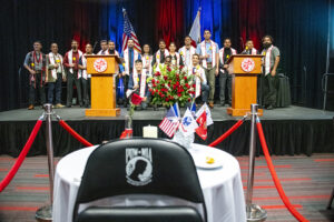 Graduates pose together on stage behind the empty table in remembrance of prisoners of war and those missing in action