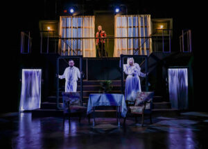 Three actors on stage in a dark, film noir-inspired production of "Hamlet."