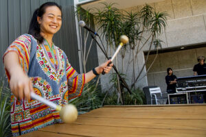 A young woman with arms in the air energetically plays the marimba.