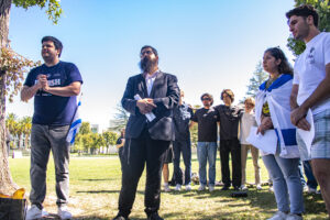 Two men stand side by side on the grass, with students in the background.