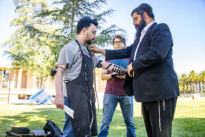 Student wearing a teffillin with black straps on his arm stands with Rabbi Chaim Brook.