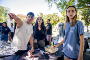 Two event workers at the event desk directing a student by pointing out where she needs to go.