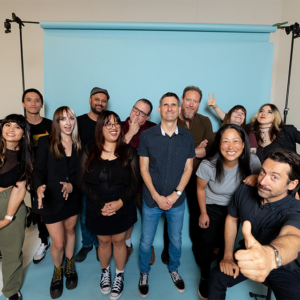 The Hopeless Records U.S staff (12) pose for a group picture in front of a blue backdrop.