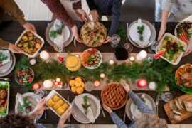 Top view of hands of family members holding plates with homemade food and desserts while serving festive table before Christmas dinner.