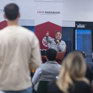 Marty Chavez, seated on stage, gestures toward a student in the foreground.