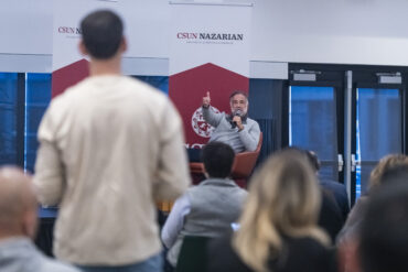 Marty Chavez, seated on stage, gestures toward a student in the foreground.