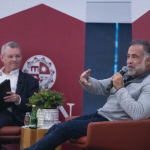 Marty Chavez gestures as he answers a question while seated on stage. Emcee Richard Schweitzer is seated to the left.