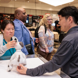 Woman stands in front of robotic dog on table.