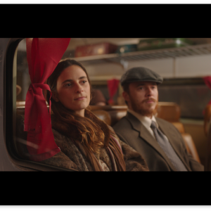 A woman and a man in period clothes as seen through a train window.