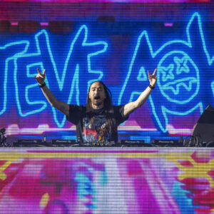 Steve Aoki plays his DJ set with his name displayed on the screen behind him.