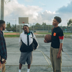 Four young men standing on an outdoor basketball court. One is holding a basketball