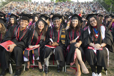A group of students, all in cap and gown, seated and smiling at the camera.