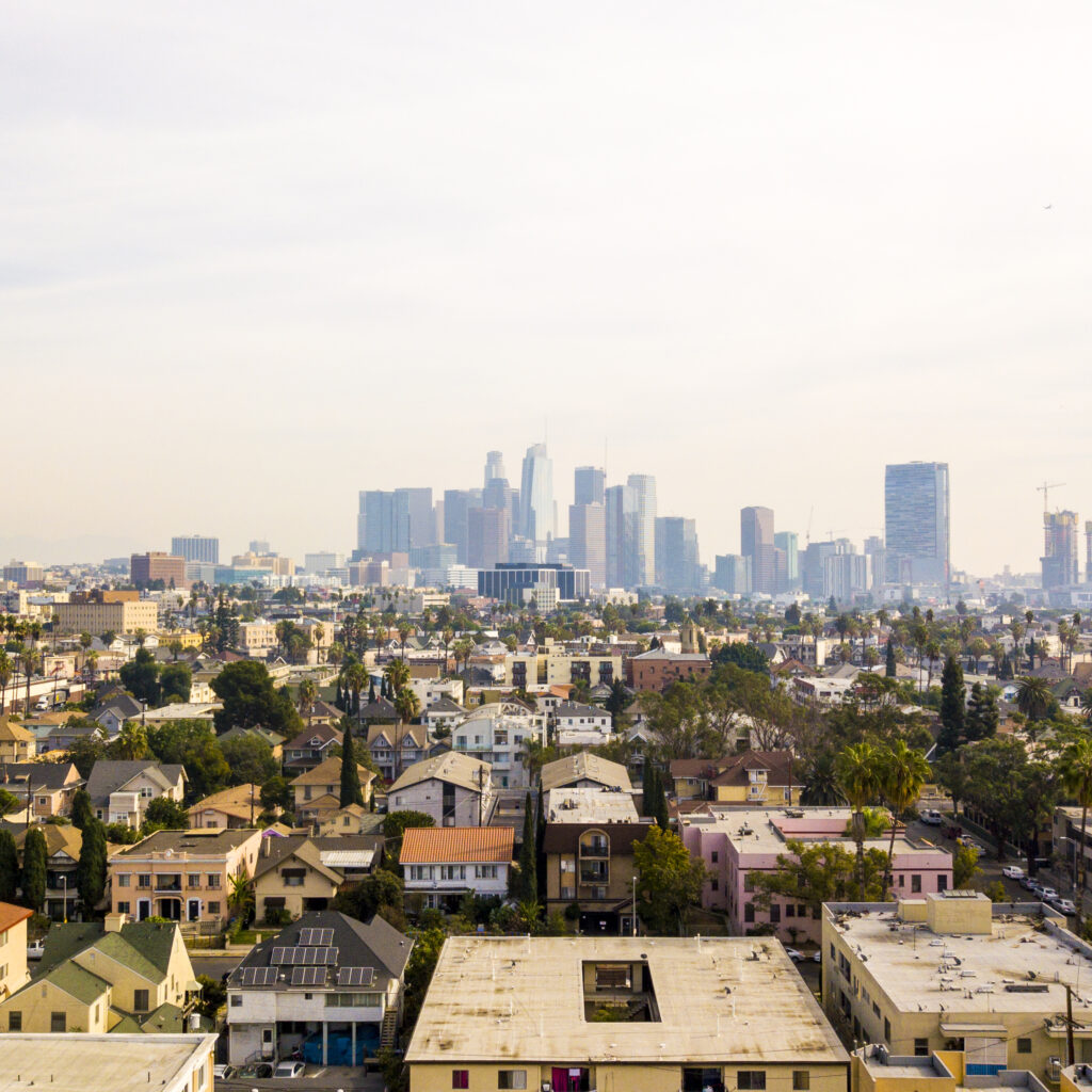 An drone shot that pictures the Los Angeles skyline in the distance with a number of houses in the foreground.