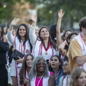 Graduates wearing sashes smile and wave.