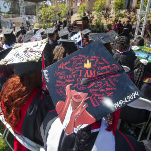Student wears elaborately decorated mortarbaord with lettering.