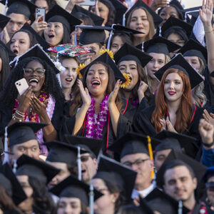 The frame is full of cheering graduates in caps and gowns at a 2024 CSUN commencement ceremony.