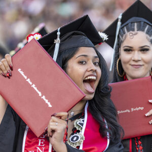 A CSUN student in cap and gown flashes her new degree.