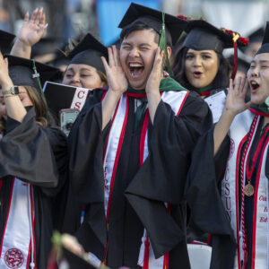 A group of students cheer at a university commencement ceremony.