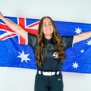 CSUN softball star Shaylan Whatman holds the Australian flag behind her and smiles.