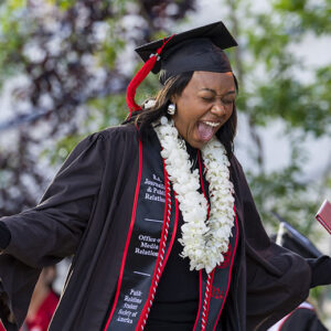Journalism/public relations graduate Sydnee Roddy yells and squeezes her eyes shut as she holds her diploma cover, on stage at the ceremony for CSUN's Mike Curb College of Arts, Media, and Communication.