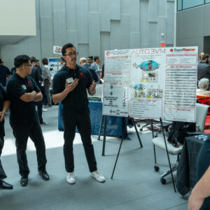 Students stand around a poster presentation of their invention.
