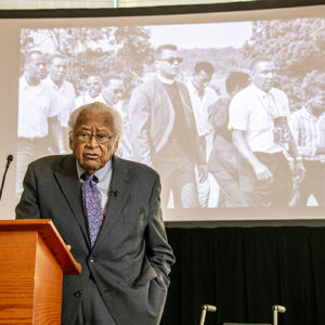 The Reverend James Lawson stands at a podium in front a large screen displaying a photo of him with Martin Luther King, Jr.