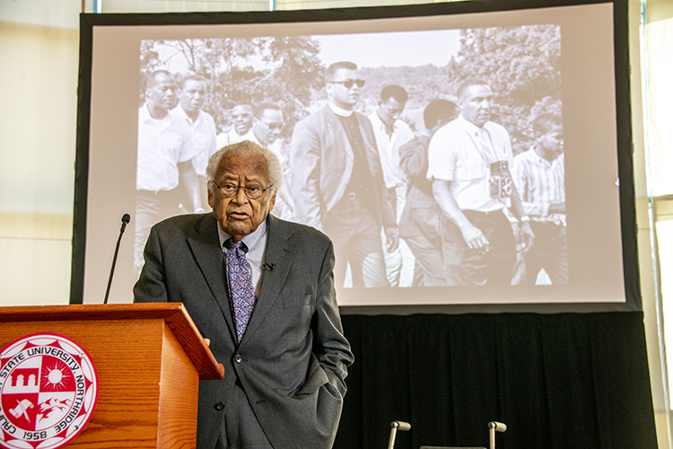 The Reverend James Lawson stands at a podium in front a large screen displaying a photo of him with Martin Luther King, Jr.
