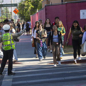 Traffic officer in a bright yellow safety vest guides students across the street.
