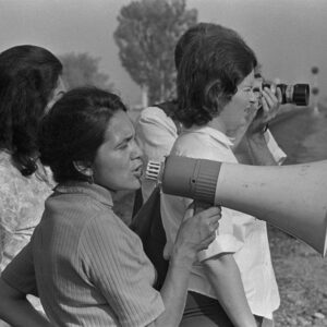 Image of a young Dolores Huerta speaking with a megaphone standing with other women