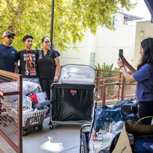 Jose Garcia poses with his Mom and Dad outside his dorm while his aunt snaps a photo on her camera.