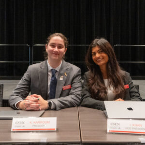 Associated Students President Katie Karroum and Vice President Iman Khan sit at a table behind signs that read their names and roles.