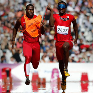 Guide runner and alumnus Wesley Williams and blind sprinter Lex Gillette hold a short tether cord, run down the track at the 2020 Tokyo Paralympics.