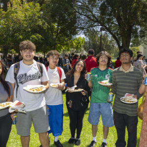 Seven students pose for a photo on Bayramian Hall Lawn while holding plates of tacos and watermelon.