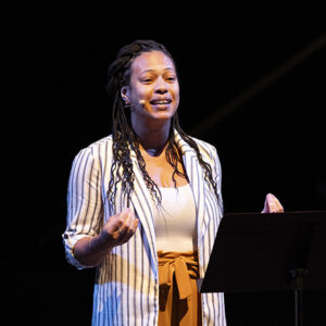 Larissa Gayton stands on stage, in front of lectern.