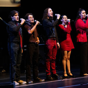 Five people, dressed in red and black, stand on stage singing.