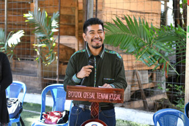 Giovanni Batz stands smiling, holding a microphone at a podium