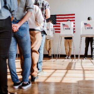 A line of people are lining up to vote for the election at the voting booths in the background.