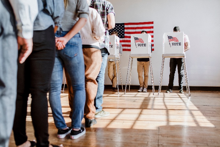 A line of people are lining up to vote for the election at the voting booths in the background.