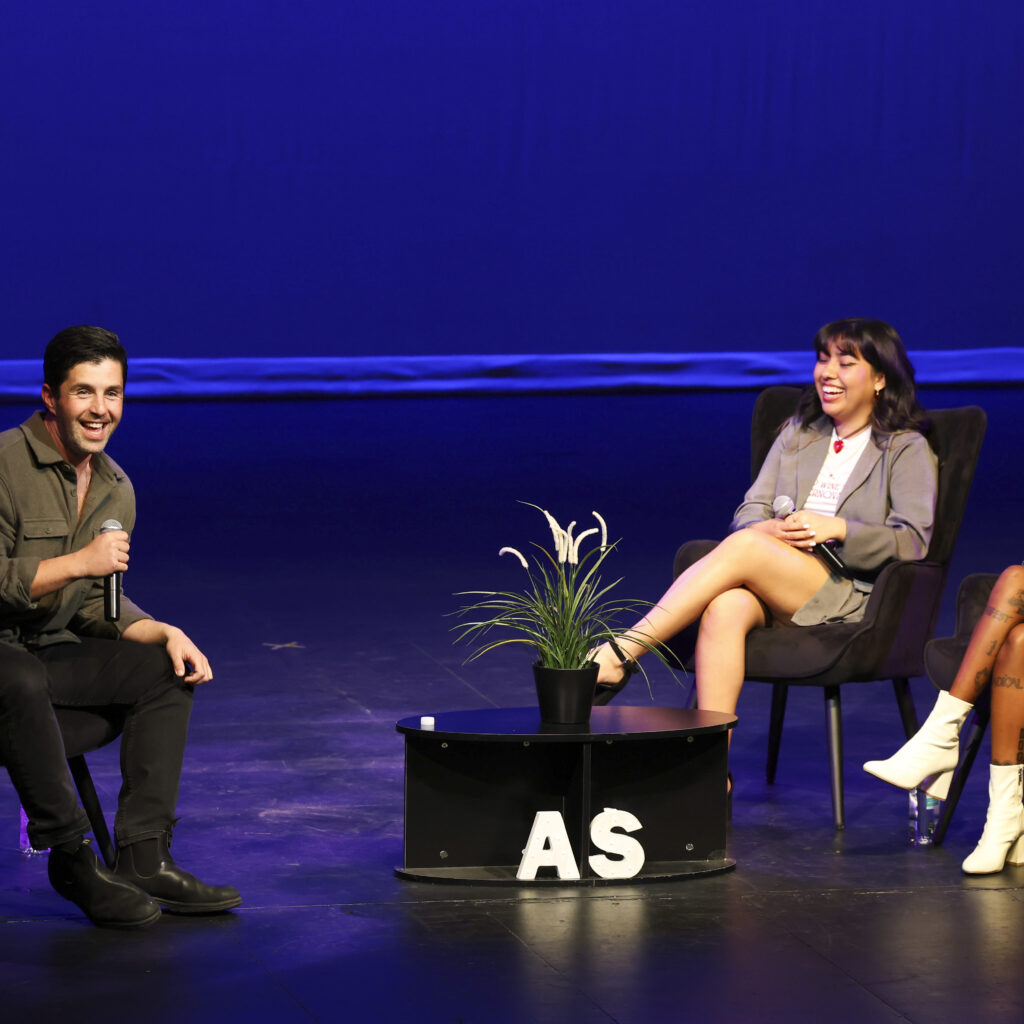 Actor Josh Peck sits on stage, smiling, across from two moderators on. stage at the Plaza Del Sol Performance Hall.