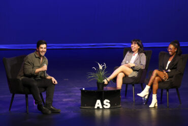 Actor Josh Peck sits on stage, smiling, across from two moderators on. stage at the Plaza Del Sol Performance Hall.