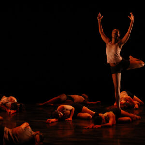 Image of one dancer standing with arms upraised while others lay before him.