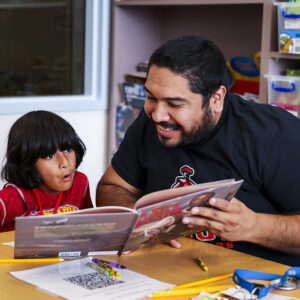 A young child looks impressed as a teacher shows him pages of a book.