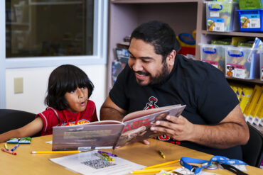 A young child looks impressed as a teacher shows him pages of a book.