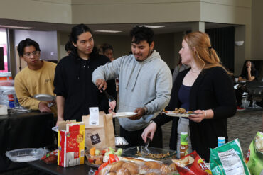 Students and staff members gather around a buffet table to load their plates.